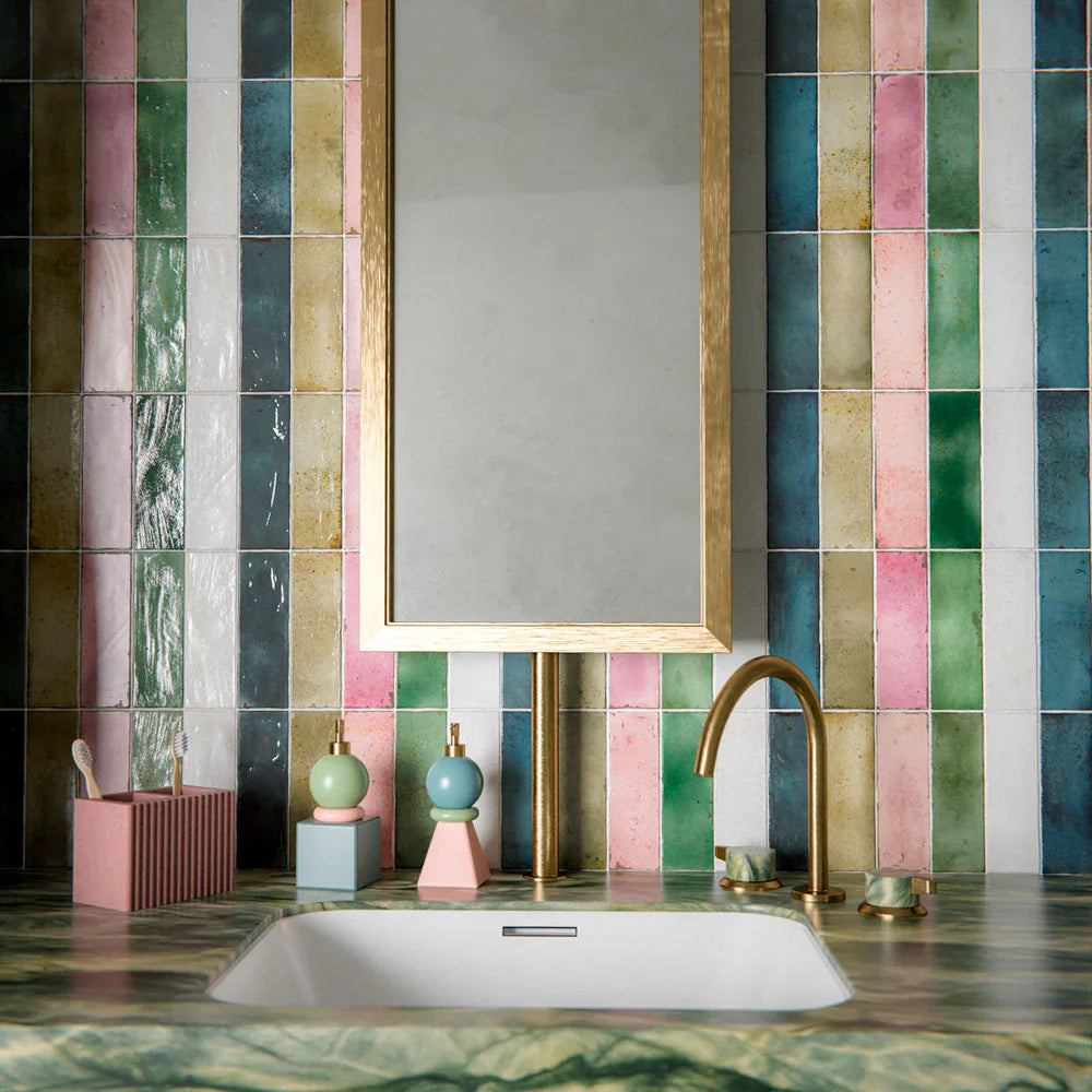 Bathroom setting featuring Fusion collection gloss brick tiles in a vertical striped layout, blending soft greens, pinks and neutrals, paired with a marble vanity and brass fittings for a vibrant, design-led finish.
