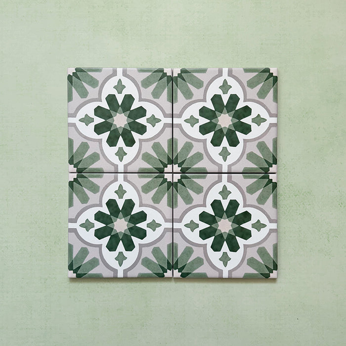 Flatlay featuring four Clarence House Jade Mini 15x15cm Victorian Moroccan-style porcelain tiles, forming a repeating geometric floral pattern in soft green, white, and grey on a light green background.
