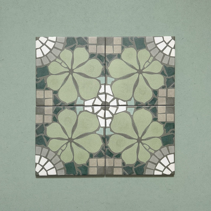 Four Bloom Green 20x20cm Moroccan-style ceramic tiles displayed together, featuring a symmetrical floral pattern in green, grey, and white tones on a soft green background.