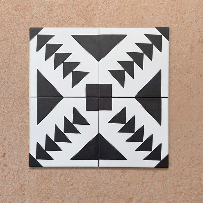 Alhambra Alkazar 20x20cm Moroccan tiles arranged in a 4-tile layout, featuring bold black triangular motifs on a crisp white background, forming a striking geometric diamond pattern on a terracotta surface.