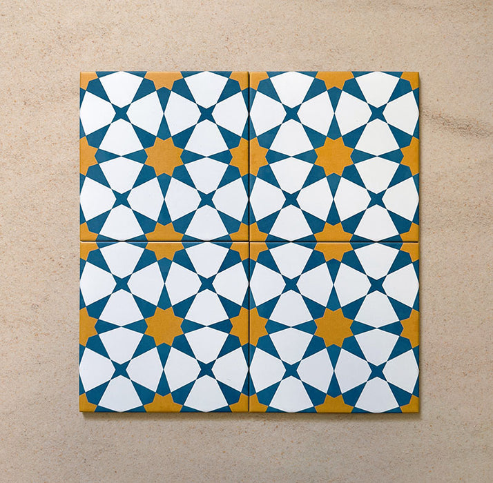 Close-up of four Agraba Sunshine 20x20cm Moroccan-style ceramic tiles arranged together, showing a geometric star pattern in blue, mustard yellow, and white on a neutral sandy background.