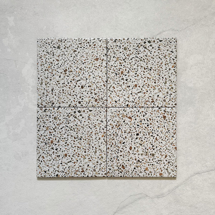 Flatlay featuring four Dino Terrazzo Blanco Dots 20x20cm terrazzo-style ceramic tiles, showing a consistent white background with multicoloured stone speckles.