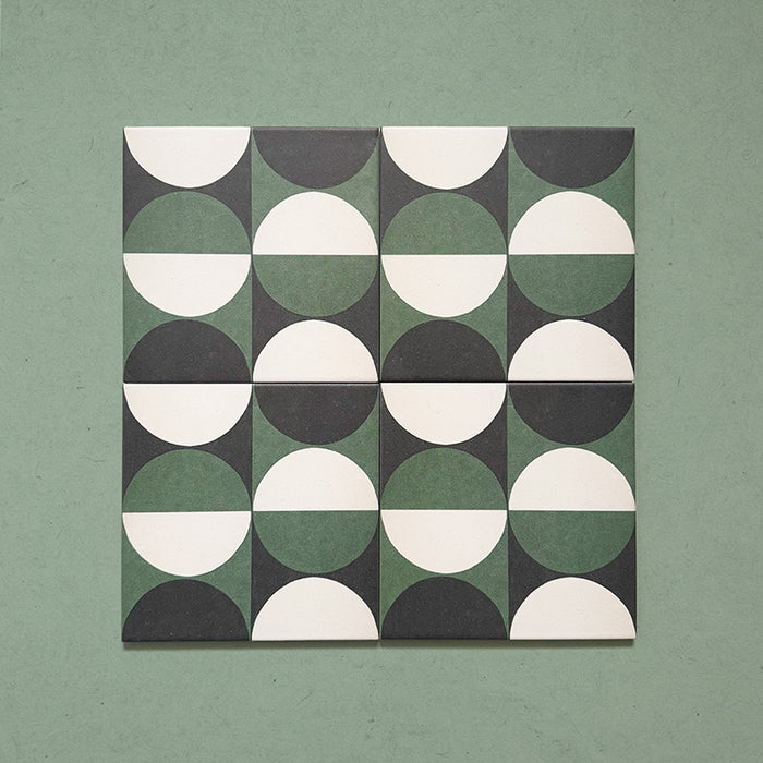 Group image showing four Geometry Circulo 20x20cm geometric patterned tiles arranged to form a circular repeat, featuring green, black, and cream semicircle motifs, photographed against a soft green textured background.