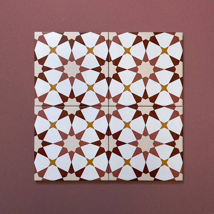 Close-up of four Agraba Cotto 20x20cm Moroccan-style ceramic tiles arranged together, highlighting the warm terracotta, beige, mustard, and white geometric star pattern on a soft burgundy background.