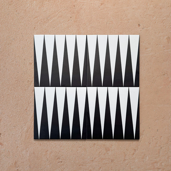 Four Alhambra Tavla 20x20cm Moroccan tiles arranged together, featuring a sharp black and white triangular design inspired by geometric patterns, displayed on a natural beige textured surface.