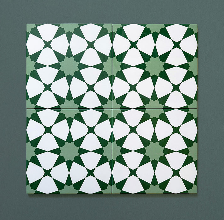 Four Agraba Green 20x20cm Moroccan-style ceramic tiles arranged together to show the seamless geometric star pattern in deep and soft green tones with white detailing on a dark green background.