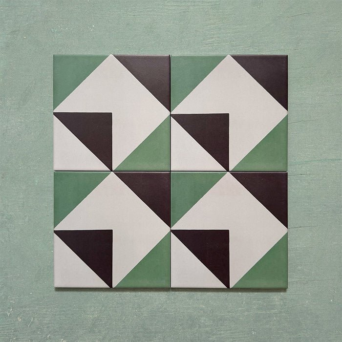 Four-piece layout of Geometry Angles Patterned Tiles, each 20cm x 20cm, featuring a geometric design of green, white, and black triangular segments forming interlocking diamond shapes, displayed on a textured green background.