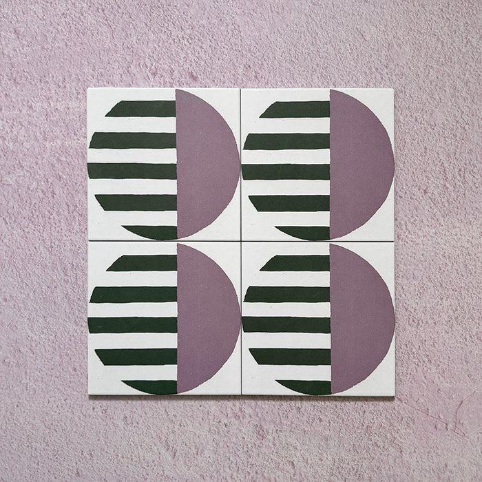 Group image showing four Geometry Seritina 20x20cm patterned tiles arranged to form a circular repeat, featuring green striped semicircles paired with mauve solid semicircles on a cream base, photographed against a textured pink background.