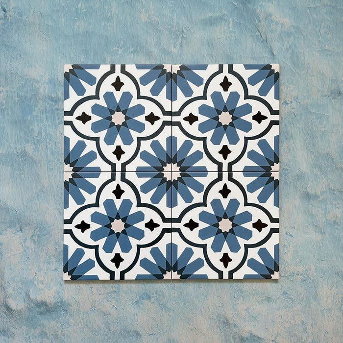 Flatlay featuring four Clarence House Azul Blue 20x20cm Victorian Moroccan-style porcelain tiles, forming a repeating blue and white geometric floral pattern on a textured blue background.