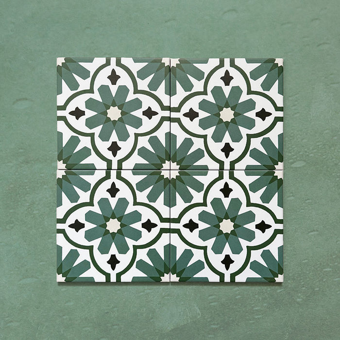 Flatlay featuring four Clarence House Verde Green 20x20cm Victorian Moroccan-style porcelain tiles, forming a repeating geometric floral pattern in green, white, and black on a textured green background.