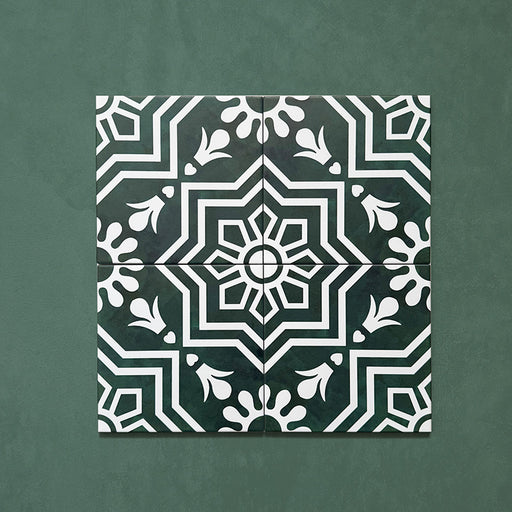 Four Brompton Victorian Green 20x20cm geometric patterned ceramic tiles displayed together, featuring a symmetrical white floral and star motif on a deep green background, shown against a matching green surface.