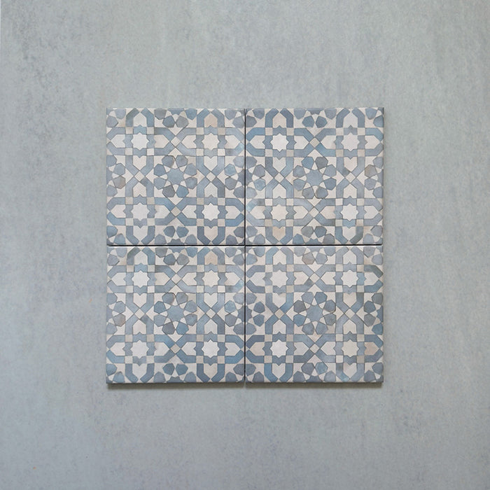 Four Bedouin Tetuan Blue Moroccan-style 15x15cm tiles arranged together, featuring an intricate geometric star and cross pattern in blue, white, and beige tones with a handcrafted effect textured finish on a pale background.