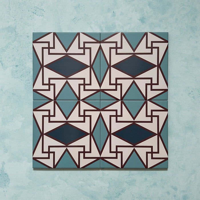 Group image showing four Geometry Iris 20x20cm patterned tiles arranged to form a continuous geometric motif in teal, navy, terracotta-red, and cream, photographed against a soft mottled aqua background.