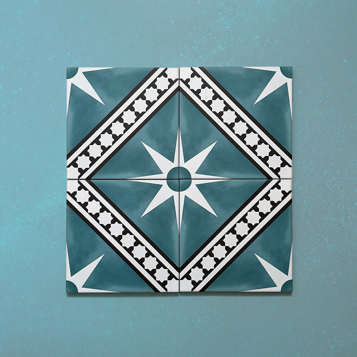 Galata Blue Moroccan Style 20x20cm layout of four tiles featuring a white eight-pointed star motif with black geometric borders and diamond framing on a deep blue background, displayed on a textured teal surface.