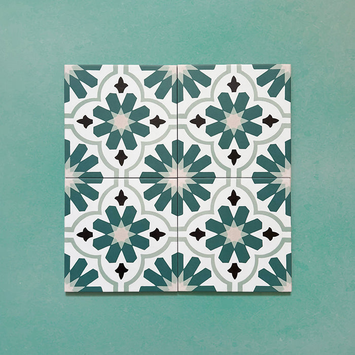 Flatlay featuring four Clarence House Teal Green 20x20cm Victorian Moroccan-style porcelain tiles, forming a repeating teal, white, and black geometric floral pattern on a green background.