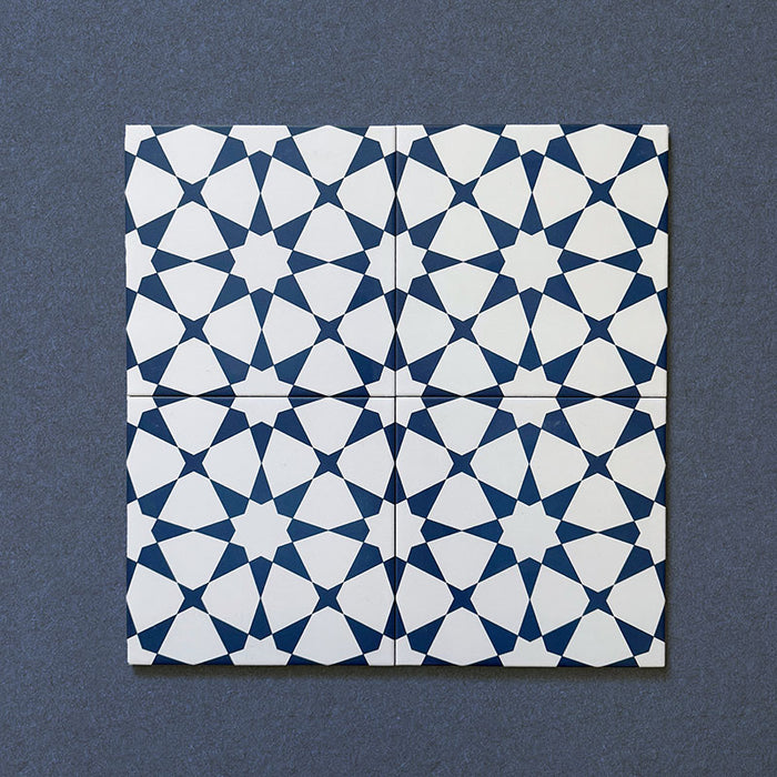 Close-up of four Agraba Navy 20x20cm Moroccan-style ceramic tiles arranged together, displaying a geometric star pattern in deep navy blue and white on a dark textured background.