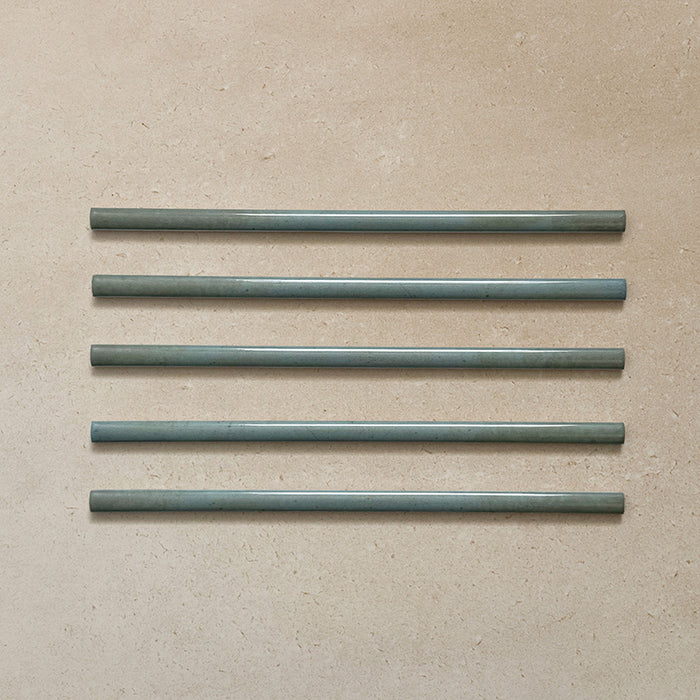 Five Izmir Celadon Green Gloss Pencil Bullnose Border Tiles 1.2x30cm displayed on a neutral beige surface, showing smooth rounded edges and a glossy green glaze.