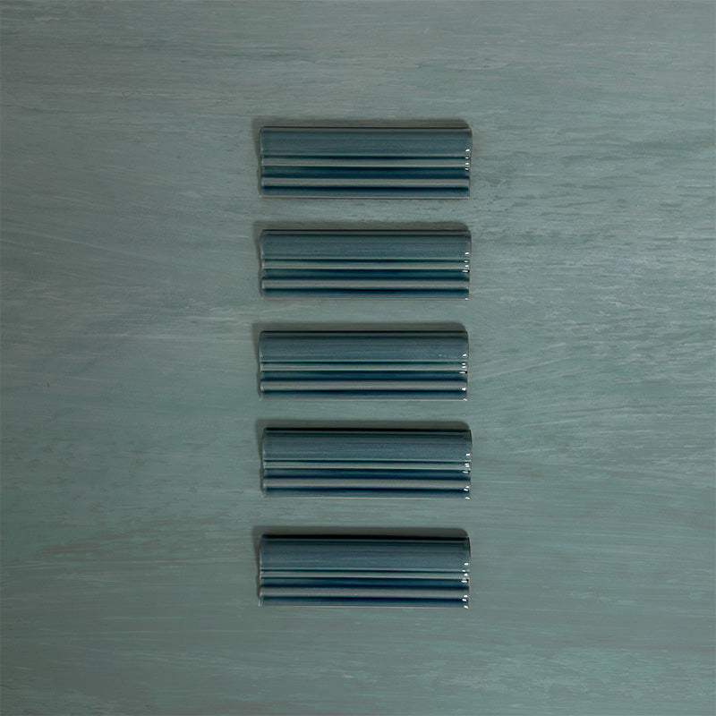 Flat lay of Finchley River Blue ceramic dado trim tiles in a 5 × 15cm format, featuring a crackle glaze finish that adds depth, texture and a decorative, classic detail to wall tile designs.