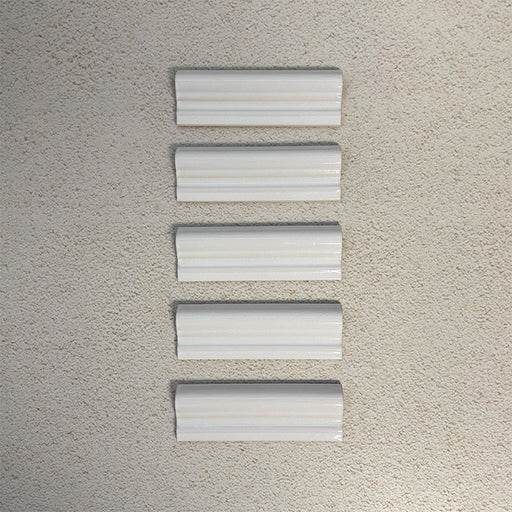 Flat lay of Finchley White ceramic dado trim tiles in a 5 × 15cm format, featuring a crackle glaze finish that adds subtle texture and a decorative, classic detail to wall tile designs.