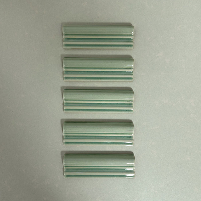 Flat lay of Finchley Lime Green ceramic dado trim tiles in a 5 × 15cm format, featuring a crackle glaze finish that adds subtle texture and a decorative, classic detail to wall tile designs.