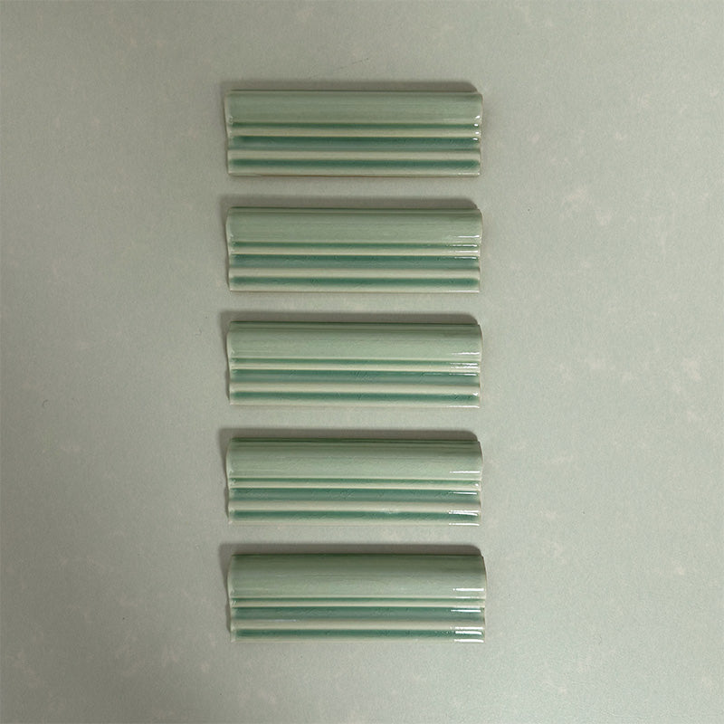 Flat lay of Finchley Lime Green ceramic dado trim tiles in a 5 × 15cm format, featuring a crackle glaze finish that adds subtle texture and a decorative, classic detail to wall tile designs.