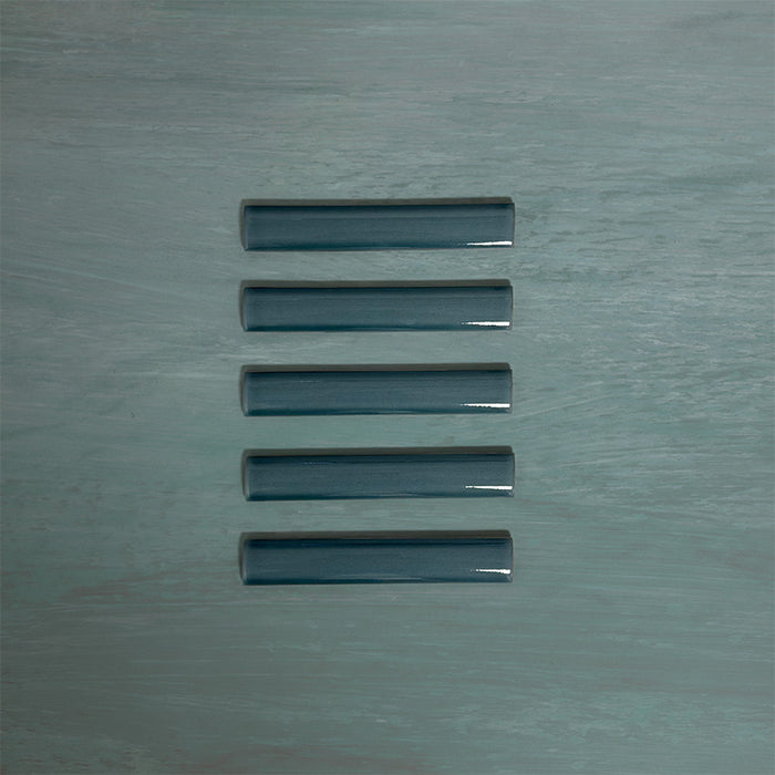 Flat lay of Finchley River Blue ceramic pencil trim tiles in a 2.5 × 15cm format, featuring a crackle glaze finish that adds subtle texture and a refined decorative edge to wall tile designs.