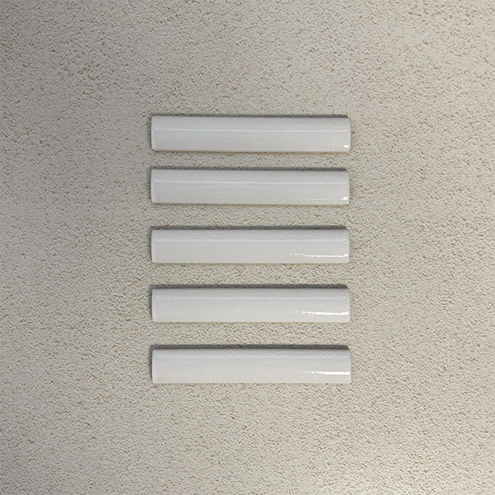 Flat lay of Finchley White ceramic pencil trim tiles in a 2.5 × 15cm format, featuring a crackle glaze finish that adds subtle texture and a refined decorative edge to wall tile installations.