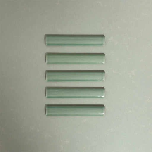 Flat lay of Finchley Lime Green ceramic pencil trim tiles in a 2.5 × 15cm format, featuring a crackle glaze finish that adds subtle texture and a refined decorative edge to wall tile designs.