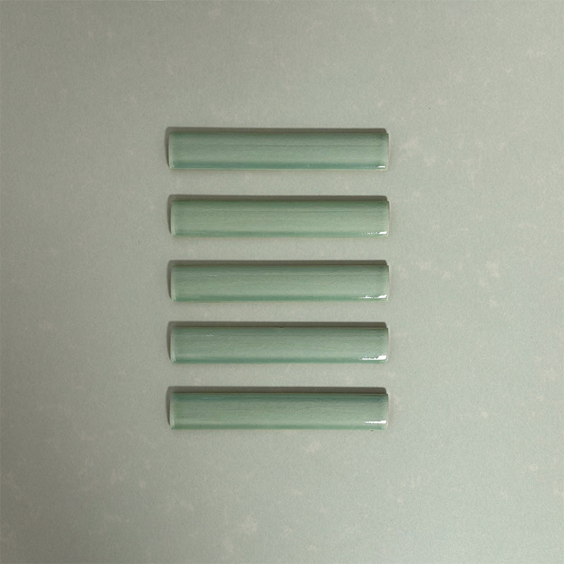 Flat lay of Finchley Lime Green ceramic pencil trim tiles in a 2.5 × 15cm format, featuring a crackle glaze finish that adds subtle texture and a refined decorative edge to wall tile designs.