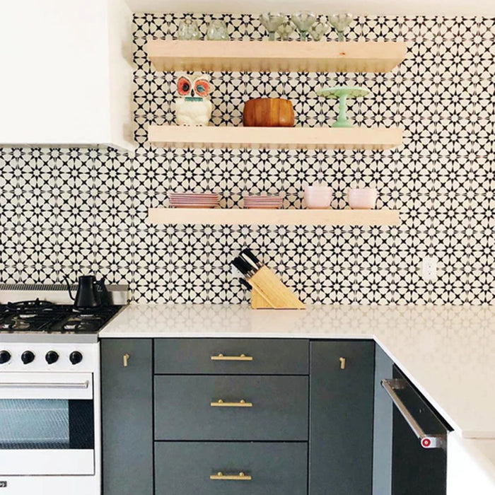 Kitchen featuring Agraba Black and White Mini 15x15cm Moroccan-style ceramic wall tiles used as a backsplash, styled with open wooden shelving, brass hardware, and modern grey cabinetry for a bold patterned look.