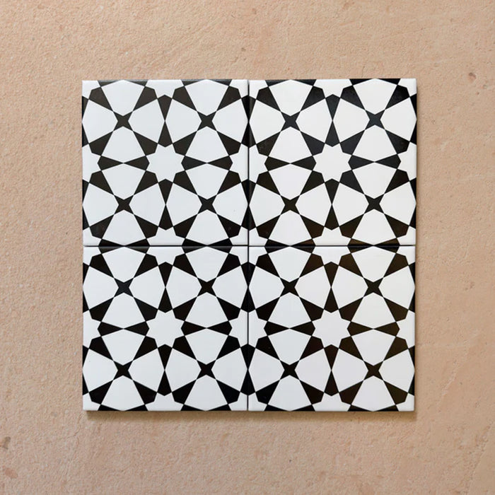 Close-up of four Agraba Black and White Mini 15x15cm Moroccan-style ceramic tiles arranged together, showing the repeating geometric star pattern and clean matt finish on a neutral surface.