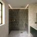 Walk-in shower featuring Agraba Natural Moroccan style patterned floor tiles, paired with sage green vertically laid wall tiles, a frameless glass shower screen and brushed brass shower fittings for a contemporary, Mediterranean-inspired bathroom.