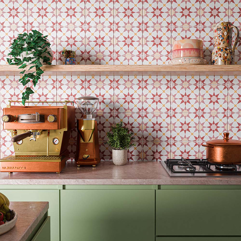 Colourful kitchen featuring Agraba Springs 20x20cm Moroccan style patterned splashback tiles, with pink, terracotta and cream geometric star motifs, paired with sage green cabinetry, copper cookware and wooden shelving.