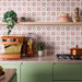 Colourful kitchen featuring Agraba Springs 20x20cm Moroccan style patterned splashback tiles, with pink, terracotta and cream geometric star motifs, paired with sage green cabinetry, copper cookware and wooden shelving.
