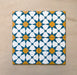 Close-up of four Agraba Sunshine 20x20cm Moroccan-style ceramic tiles arranged together, showing a geometric star pattern in blue, mustard yellow, and white on a neutral sandy background.