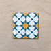 Close-up of Agraba Sunshine 20x20cm Moroccan-style ceramic tile featuring a bold geometric star pattern in blue, mustard yellow, and white on a neutral sandy background.
