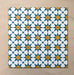 Close-up of multiple Agraba Sunshine 20x20cm Moroccan-style ceramic tiles arranged in a grid, showcasing a vibrant geometric star pattern in blue, mustard yellow, and white on a neutral sandy background.