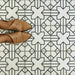 Alhambra Palacio 20x20cm Moroccan tiles with a black geometric cross pattern on a white base, shown from above with tan shoes to highlight the detailed design and matte finish.