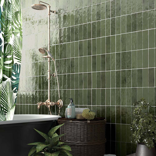 Zellij Botanical Green brick tiles, 6.5cm x 20cm, Moroccan style glazed ceramic wall tiles in rich botanical green tones with natural tonal variation, glossy finish, and handcrafted surface texture, shown in a bathroom setting with a freestanding bath, brass shower fittings, and lush green plants.