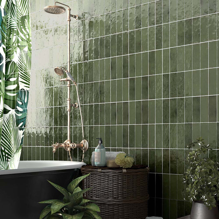 Zellij Botanical Green brick tiles, 6.5cm x 20cm, Moroccan style glazed ceramic wall tiles in rich botanical green tones with natural tonal variation, glossy finish, and handcrafted surface texture, shown in a bathroom setting with a freestanding bath, brass shower fittings, and lush green plants.