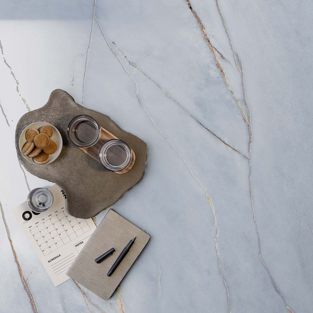 Close-up of Bassano River Blue Lux 3D 60 × 120cm marble-effect wall and floor tiles, showcasing soft blue tones with delicate gold and grey veining and a luxurious polished contemporary finish.