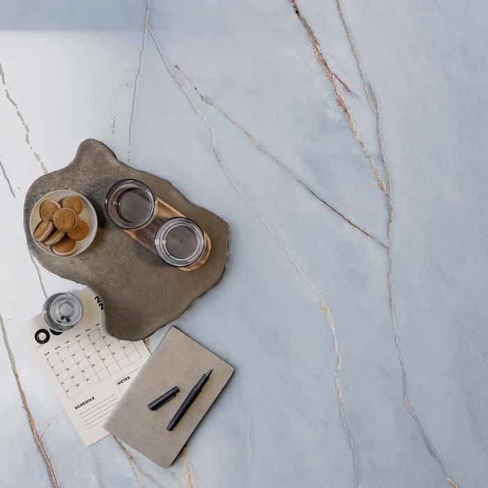 Close-up of Bassano River Blue Lux 3D 60 × 120cm marble-effect wall and floor tiles, showcasing soft blue tones with delicate gold and grey veining and a luxurious polished contemporary finish.