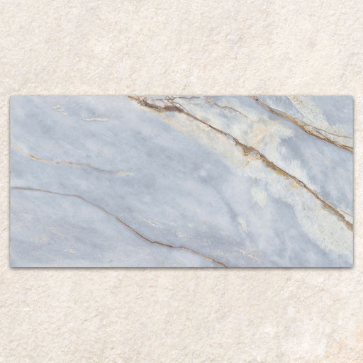 Single tile display of Bassano River Blue Lux 3D 60 × 120cm marble-effect wall and floor tiles, featuring soft blue tones, flowing gold and beige veining, and a polished finish inspired by luxurious natural stone.