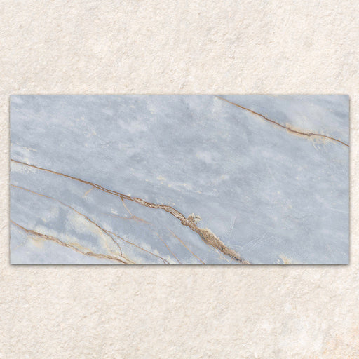 Single tile display of Bassano River Blue Matt 60 × 120cm marble-effect wall and floor tiles, featuring soft blue tones, flowing gold and beige veining, and a smooth matt finish inspired by elegant natural stone.
