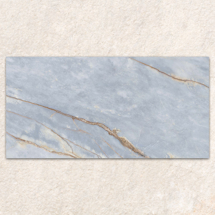 Single tile display of Bassano River Blue Matt 60 × 120cm marble-effect wall and floor tiles, featuring soft blue tones, flowing gold and beige veining, and a smooth matt finish inspired by elegant natural stone.