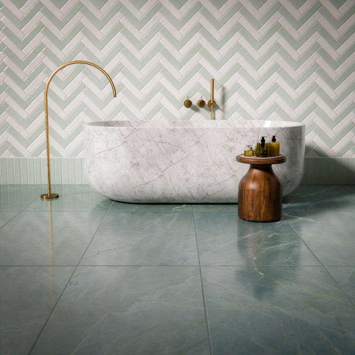 Bathroom interior featuring Bassano Sea Green Lux 3D 60 × 120cm marble-effect wall and floor tiles, paired with a freestanding marble bath, brass fittings, soft green tones, and herringbone wall tiles for a calming contemporary space.