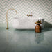 Bathroom interior featuring Bassano Sea Green Lux 3D 60 × 120cm marble-effect wall and floor tiles, paired with a freestanding marble bath, brass fittings, soft green tones, and herringbone wall tiles for a calming contemporary space.