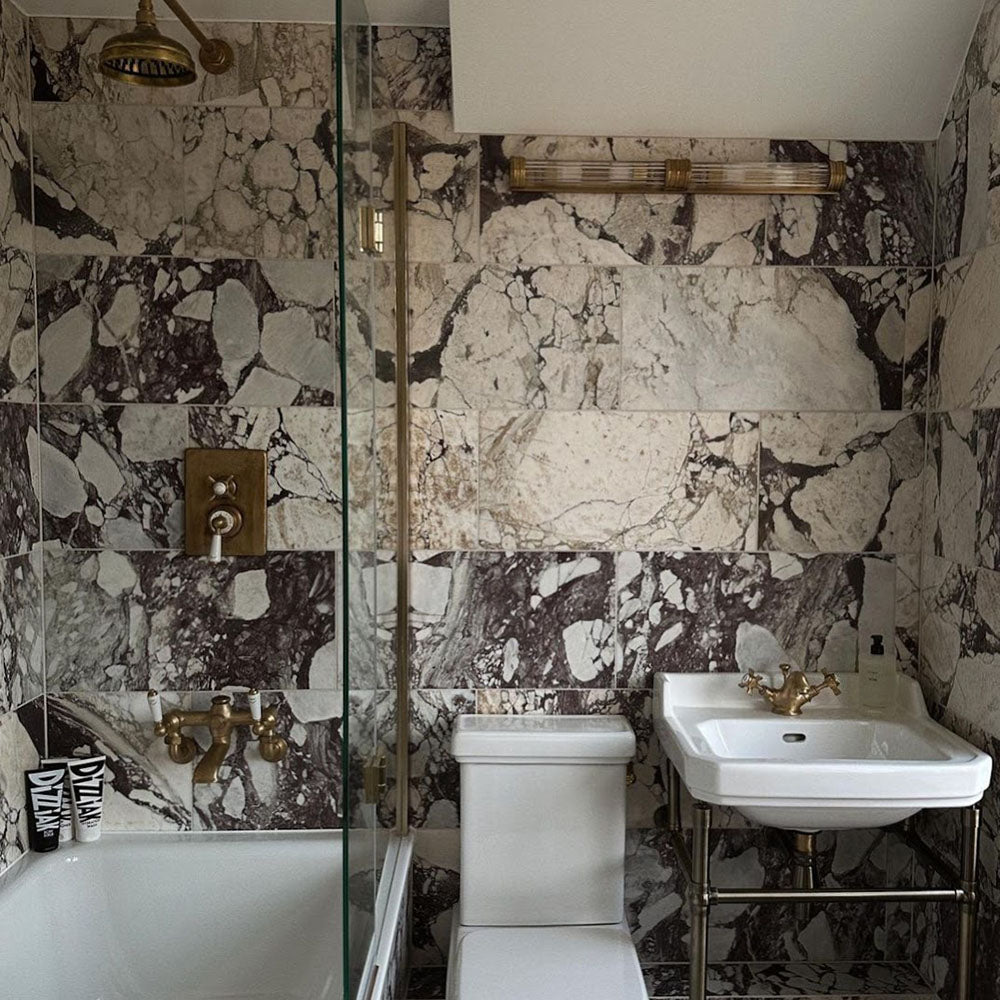 Bathroom setting featuring Fitzrovia Viola 30.5x61cm natural marble tiles with a honed finish, showcasing a white base with bold burgundy and deep grey veining, paired with brass fittings for a rich, statement finish.