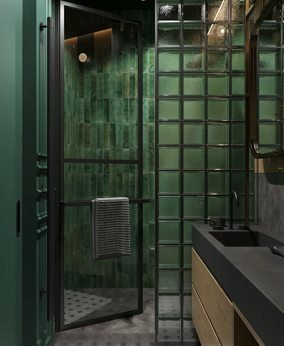 Bathroom setting featuring Mizu Green 6x24cm porcelain wall and floor tiles, showcasing rich tonal variation in deep green hues, paired with glass blocks, dark stone finishes and wood cabinetry for a moody, contemporary, design-led space.