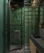 Bathroom setting featuring Mizu Green 6x24cm porcelain wall and floor tiles, showcasing rich tonal variation in deep green hues, paired with glass blocks, dark stone finishes and wood cabinetry for a moody, contemporary, design-led space.